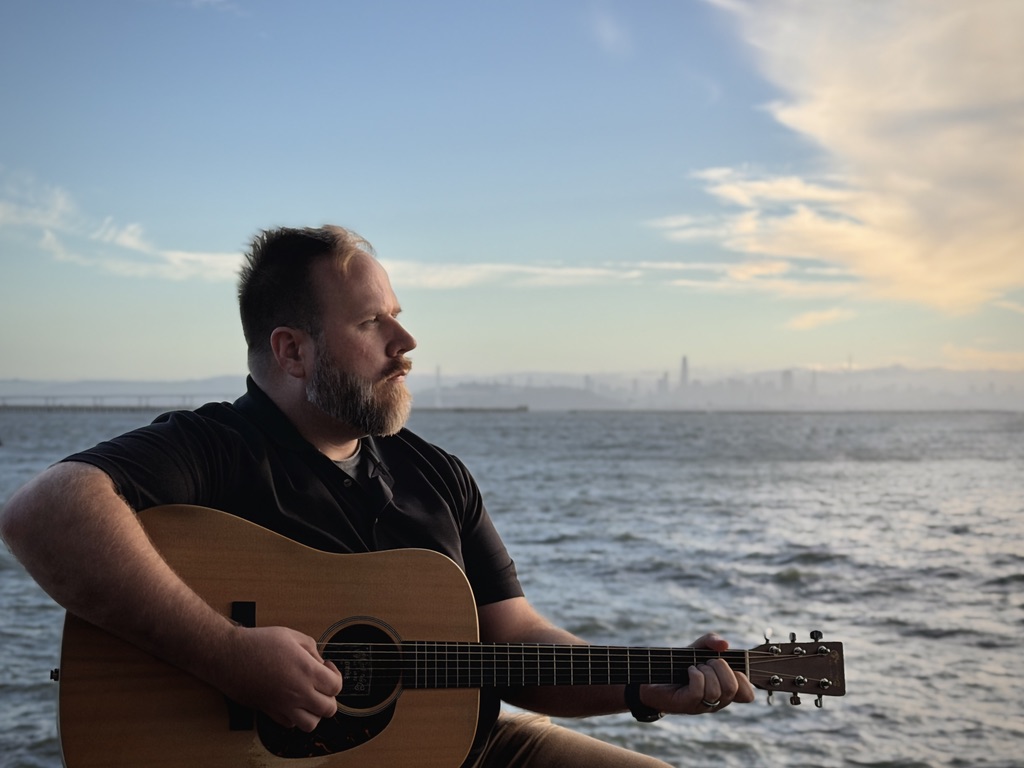 Robert Sullivan playing guitar by the waterfront